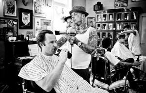 Een zwart-wit foto waarin een man wordt op een ouderwetse wijze geschoren met een open scheermes door hipster kapper met tatoeages.